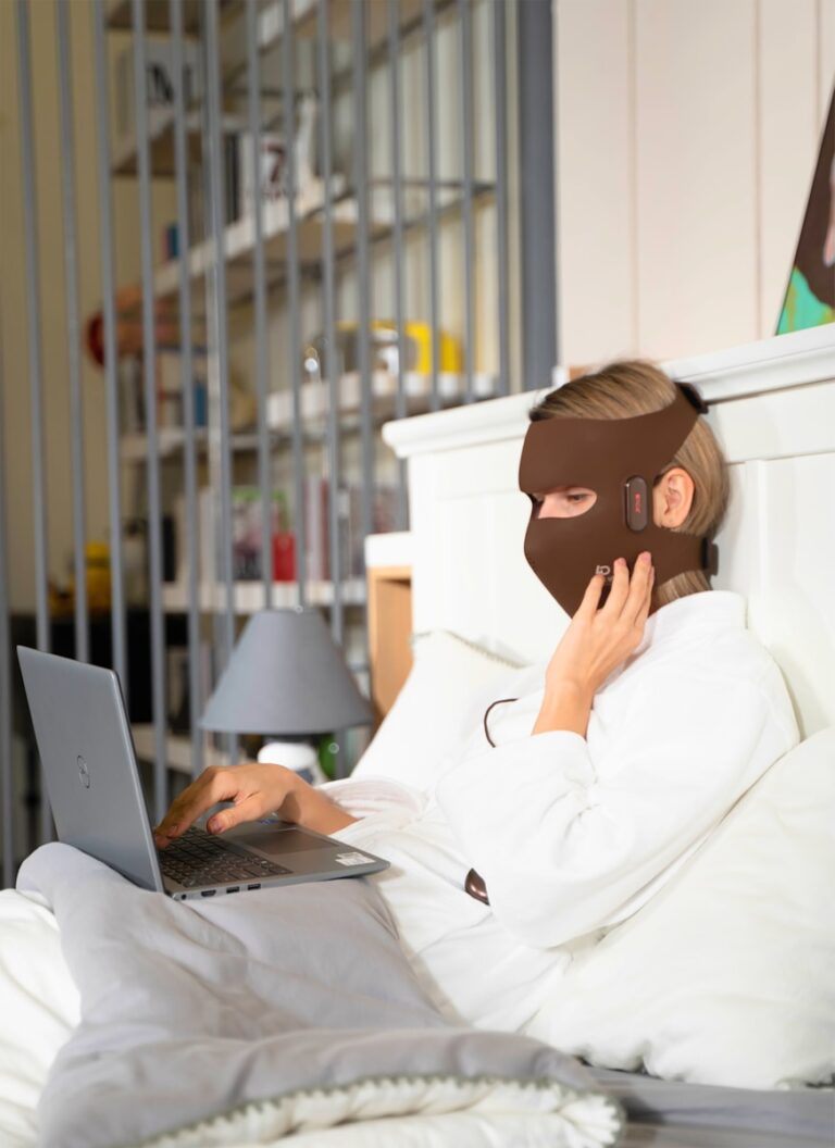 A person in a bed with a mask on and a laptop